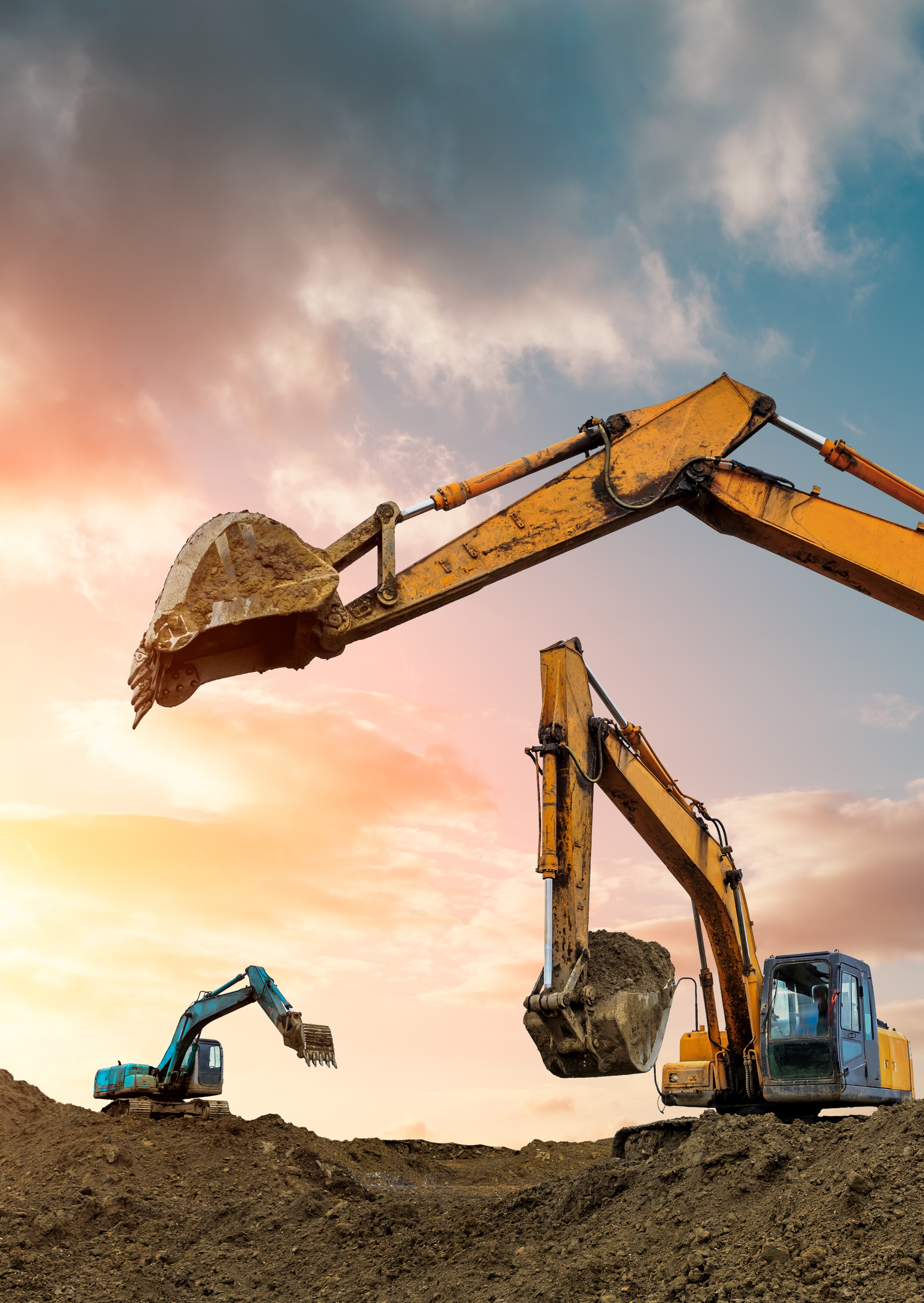 Three diggers on dirt against sunset