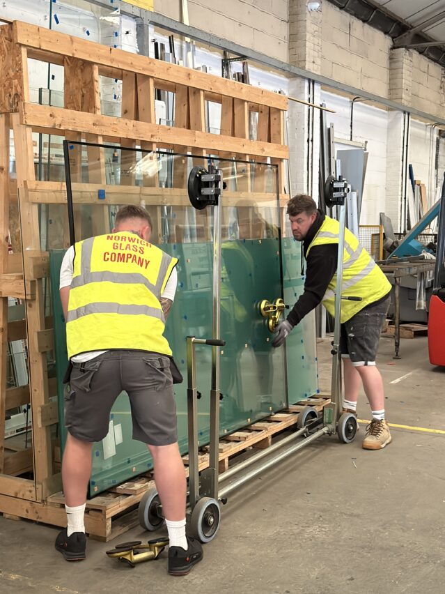 Two men in high vis vets carrying a large pane of glass