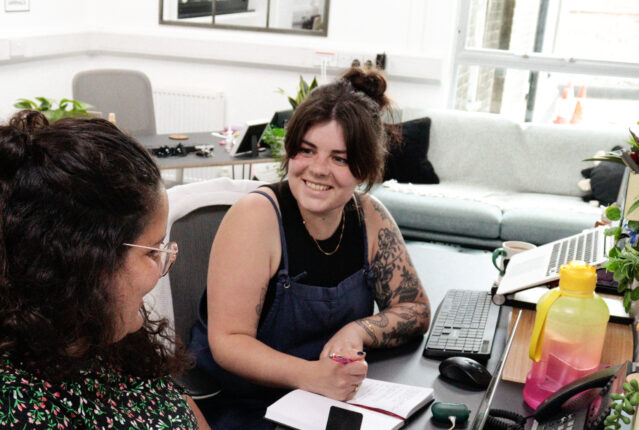 Two brunette women working at their desks and smiling