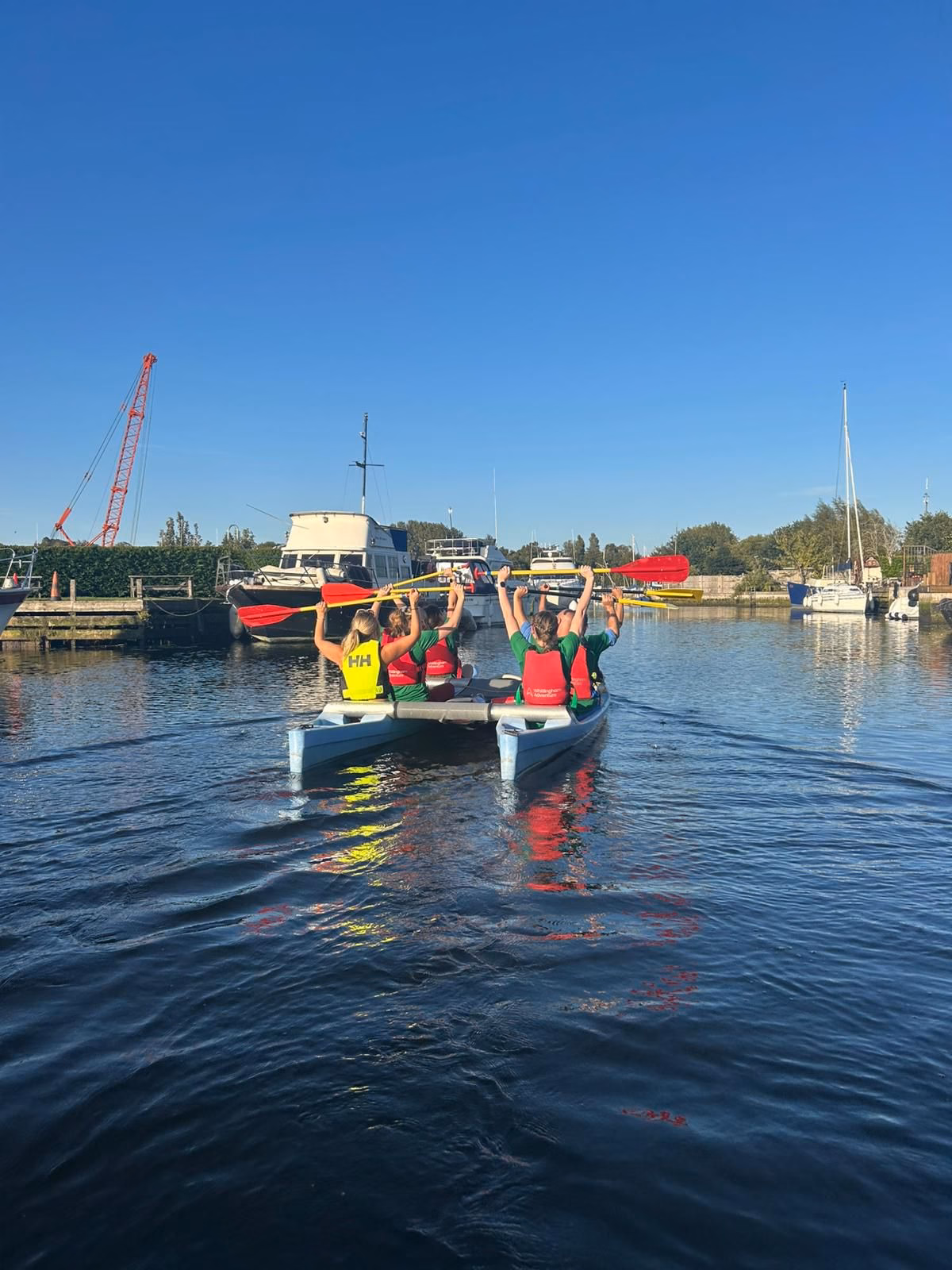 Team at the end of challenge on canoe in water, holding paddles above their heads